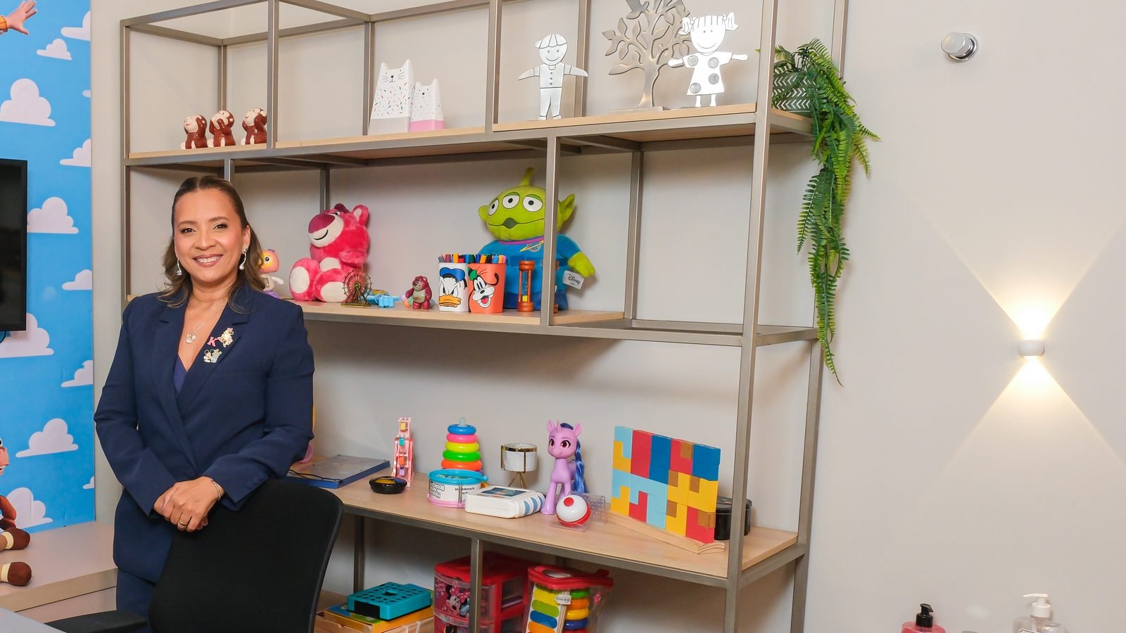 Kennya Martins, psicóloga infantil, ao lado da estante de jogos e brinquedos da sala de atendimento