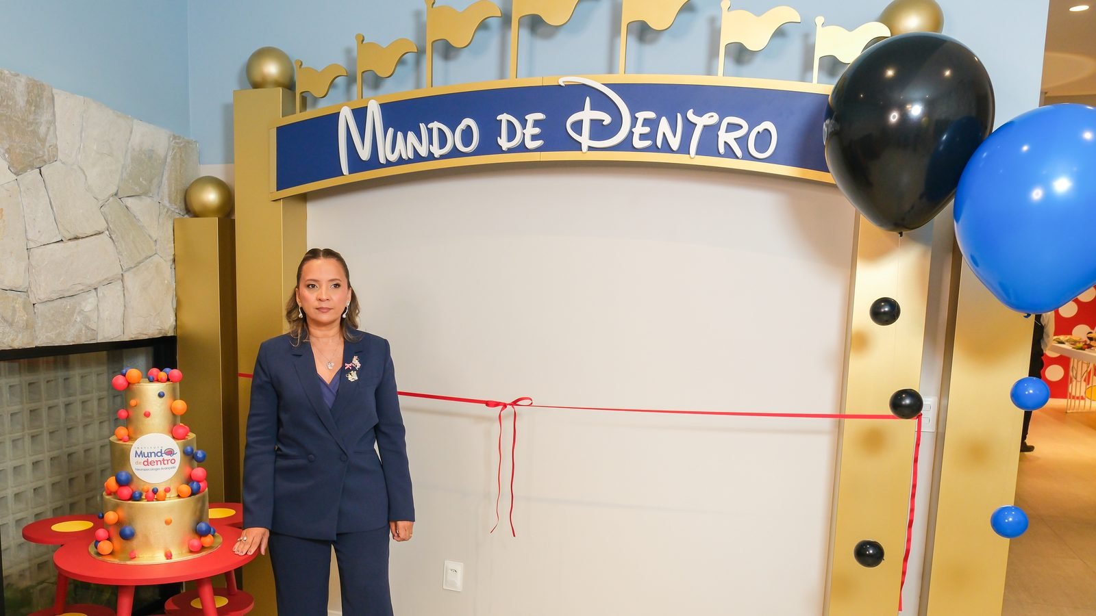 Kennya Martins diante do portal de entrada do Instituto Mundo de Dentro, ao lado do bolo de inauguração