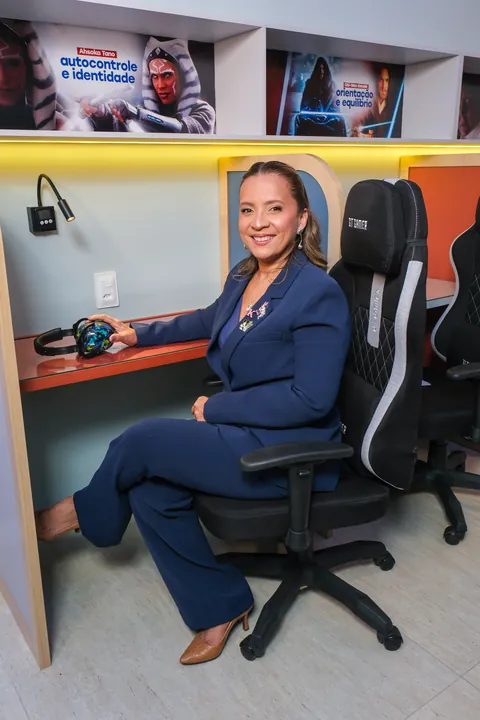 Kennya Martins sentada em uma cabine da sala de estudo do Instituto Mundo de Dentro, com um fone de ouvido sobre a mesa